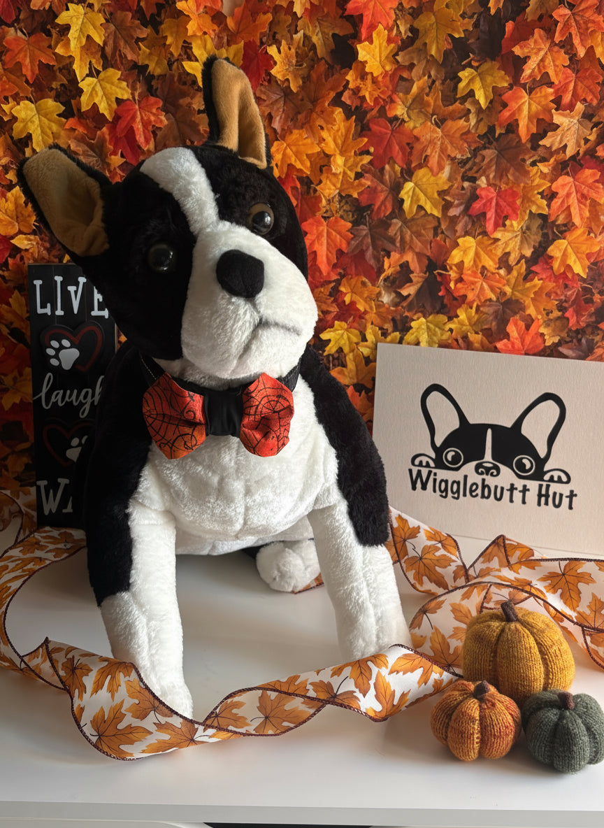 Plush dog toy with a bow tie on a white background, next to a sign with a logo.