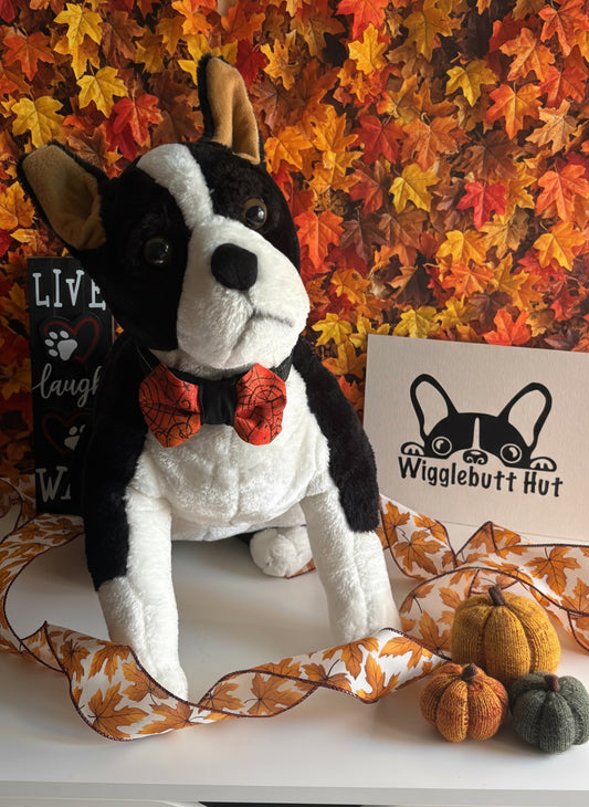 Plush dog toy with a bow tie on a white background, next to a sign with a logo.