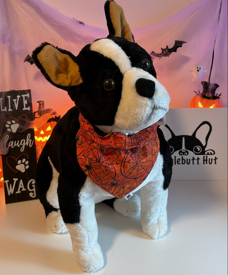 Stuffed dog toy with a Halloween bandana in front of a 'Live Laugh Wag' sign and a logo.